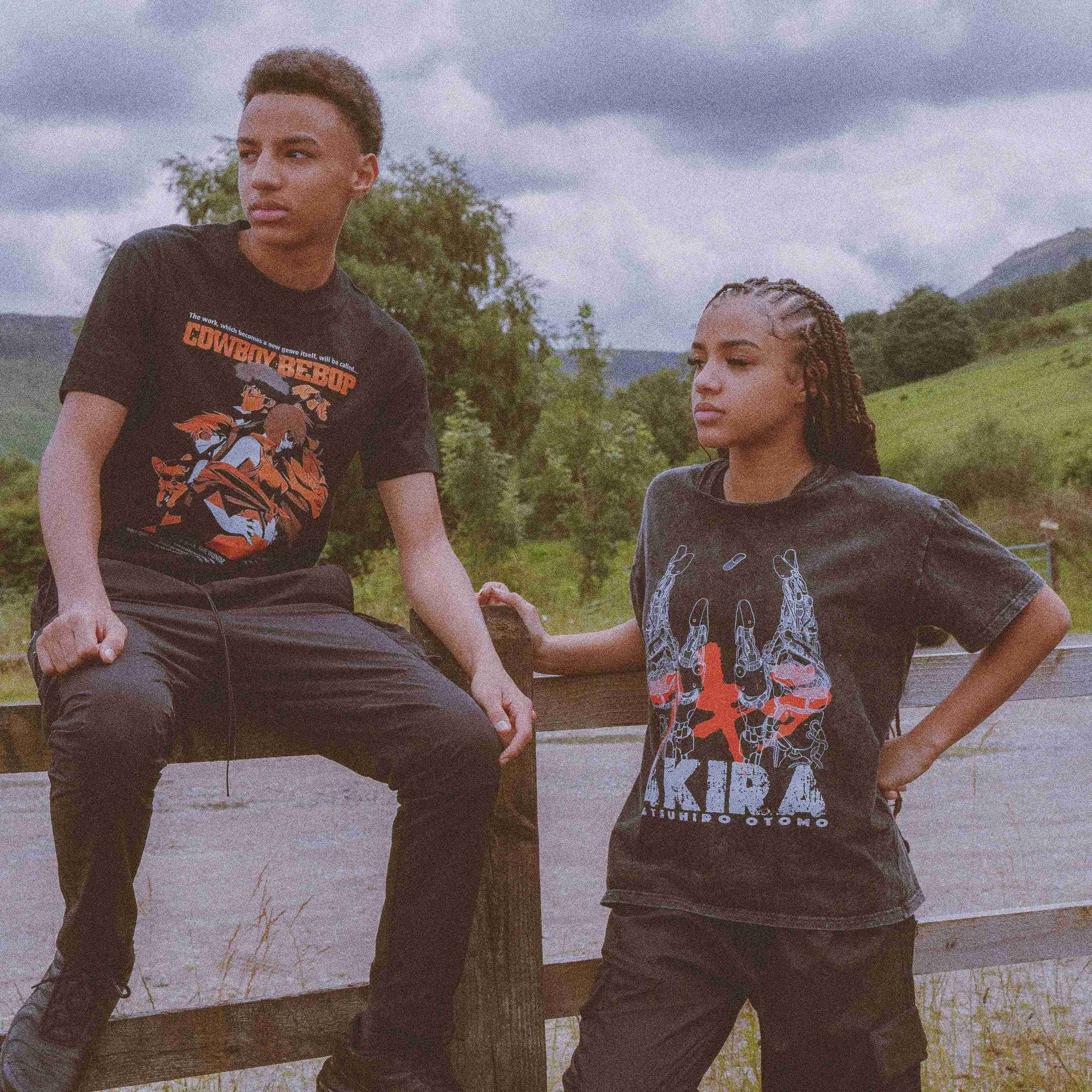 Two Models wearing Cowboy Bebop and Akira graphic T-shirts standing outdoors with cloudy sky and greenery in background