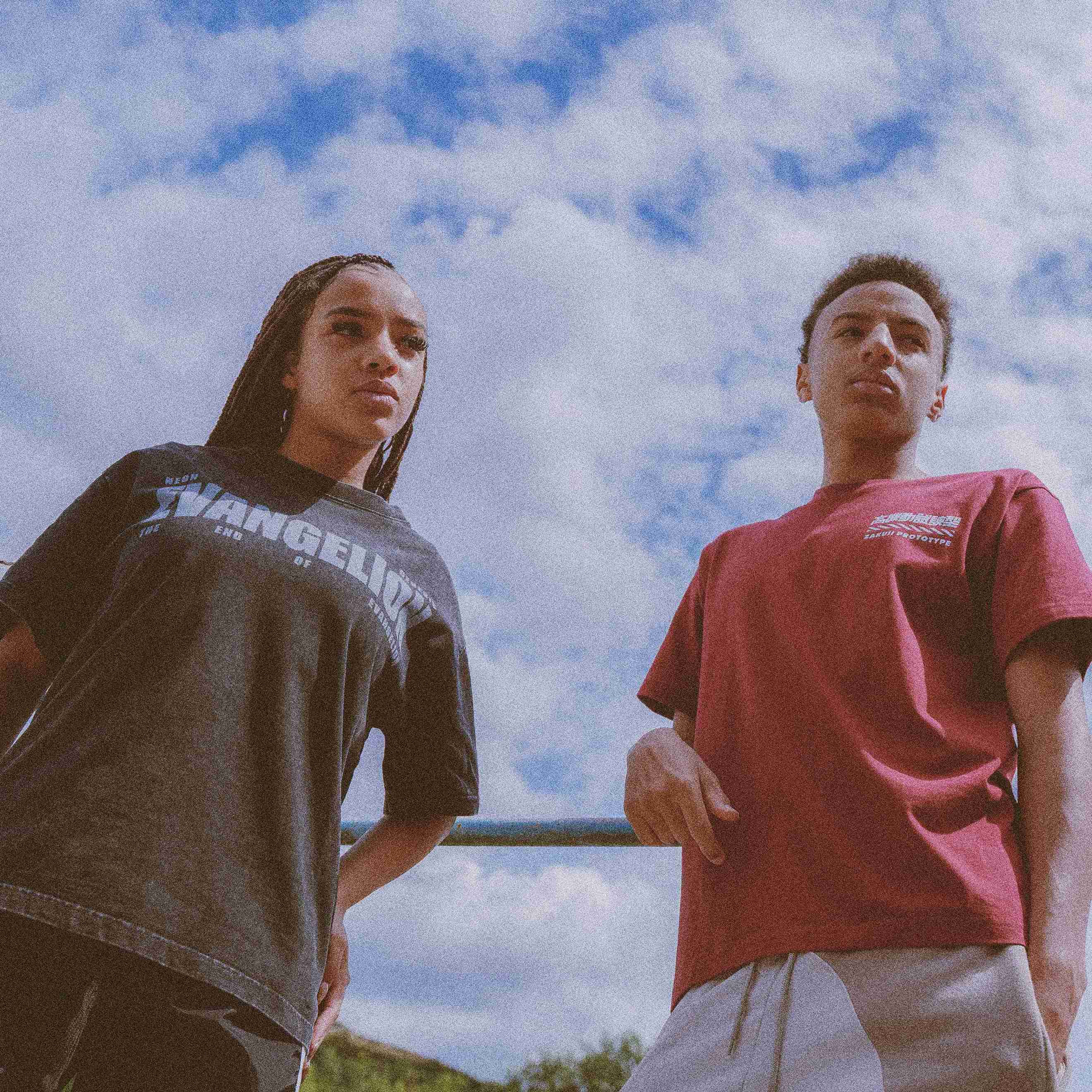 Two models wearing Evangelion & Gundam T Shirts while leaning against a pole