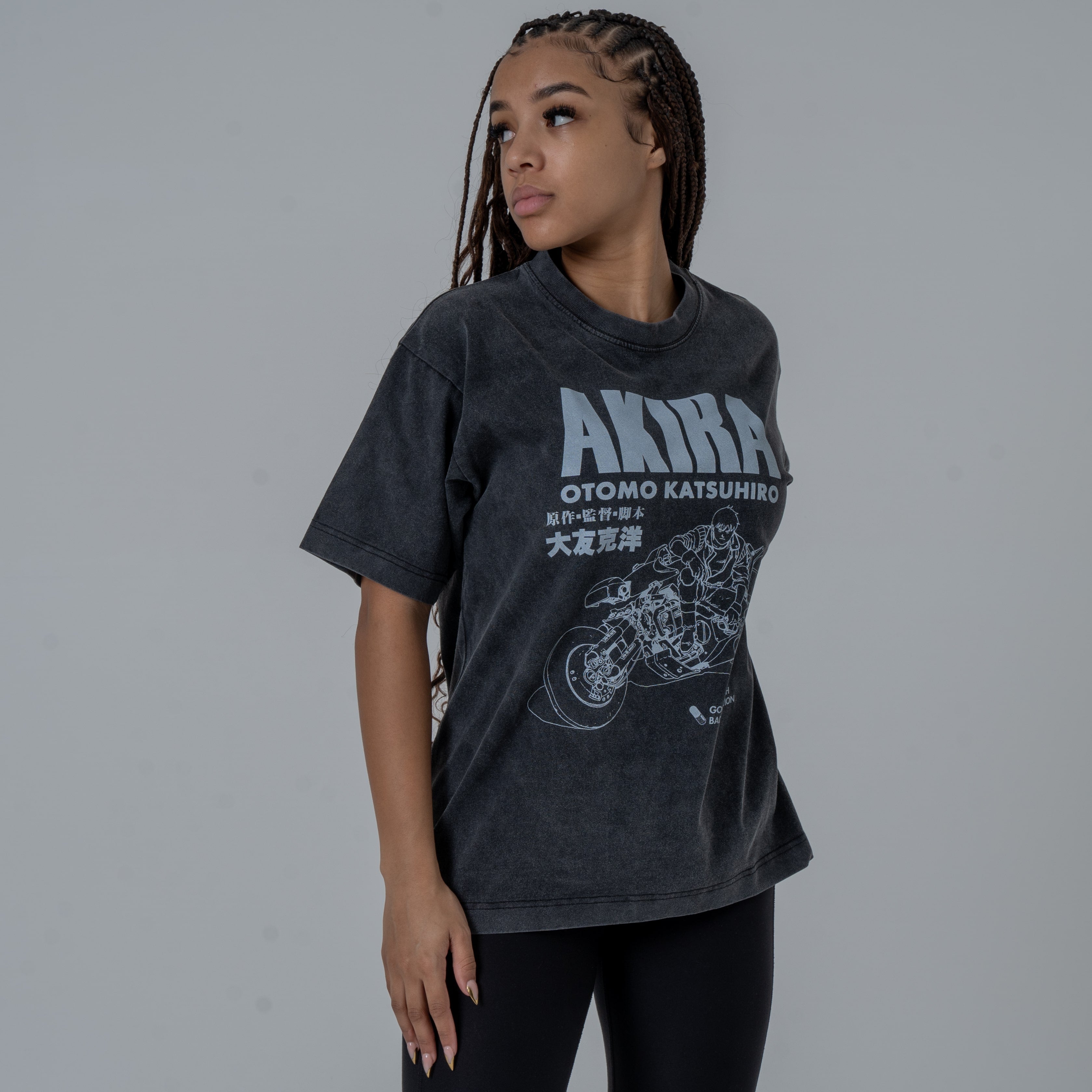 Female model in a studio wearing a black vintage-washed anime T-shirt featuring a white Akira graphic with Kaneda riding his iconic motorcycle, while looking to the left.