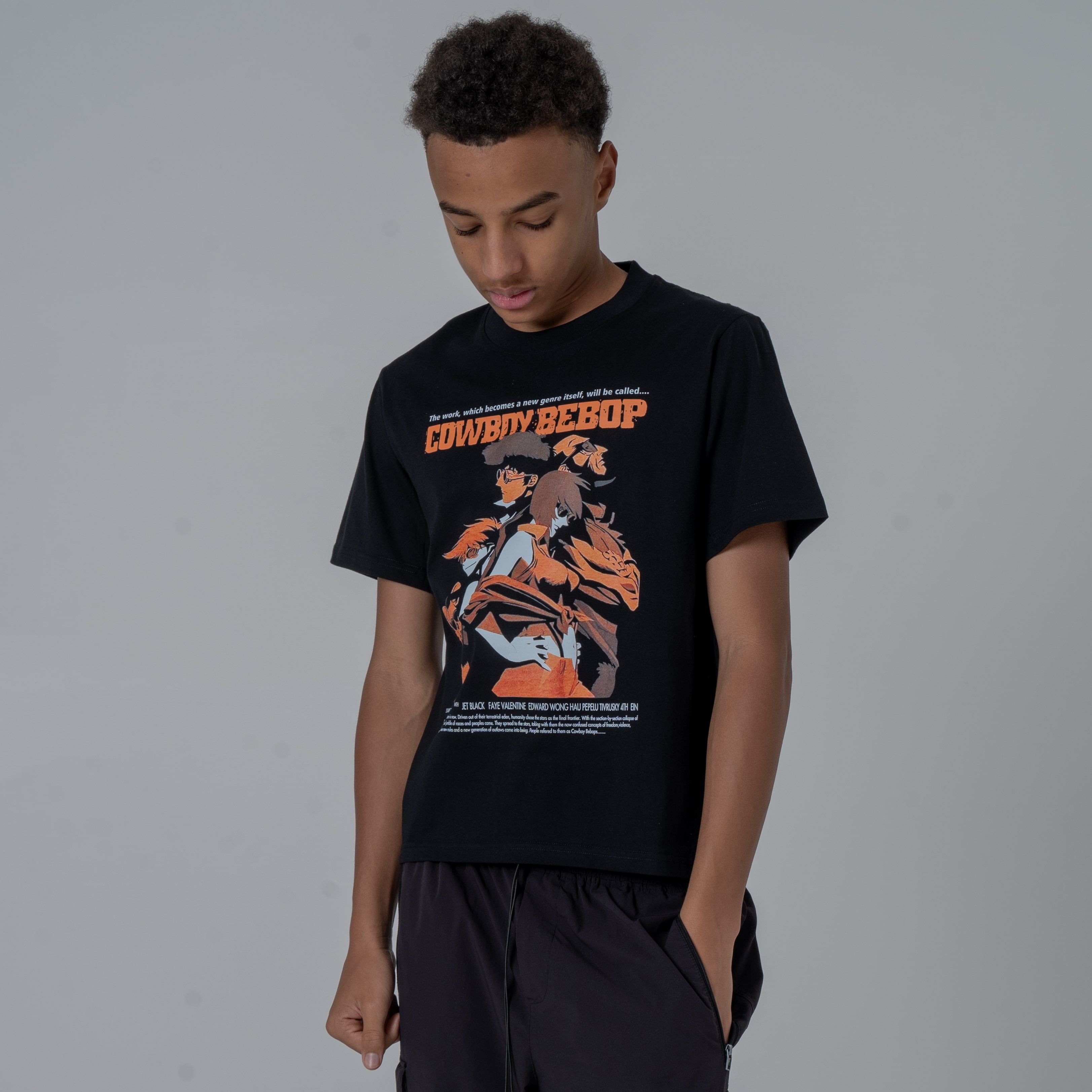 Half body shot of a male model looking down in a studio wearing anime t shirt with orange cowboy bebop graphic.