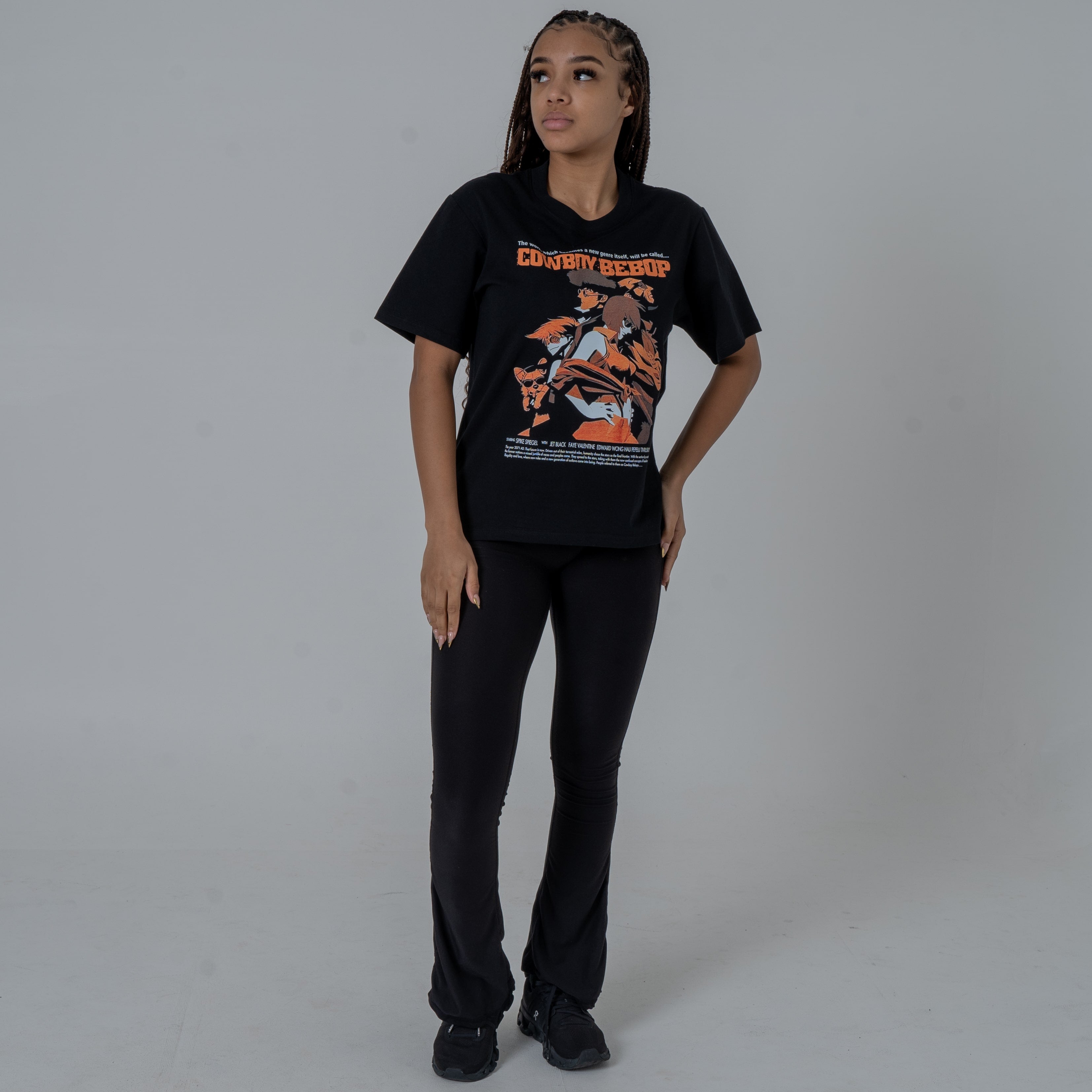 Full body shot of a female model in a studio wearing a black anime T-shirt with an orange Cowboy Bebop graphic featuring Ein, Spyke, Jet, Ed and Faye.
