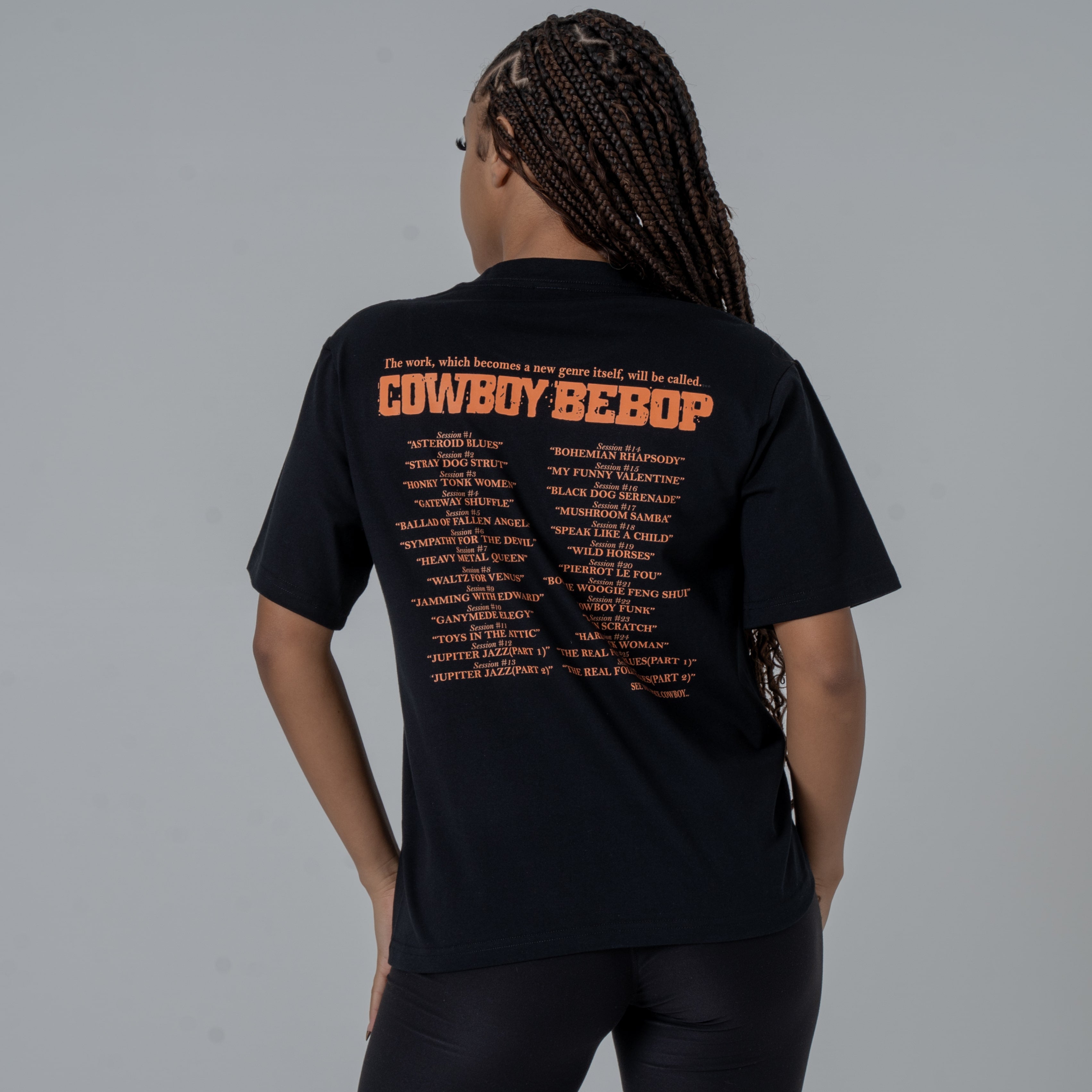 Back view of a female model in a studio wearing a black anime T-shirt with an orange Cowboy Bebop graphic featuring a list of episode titles in vintage-style.