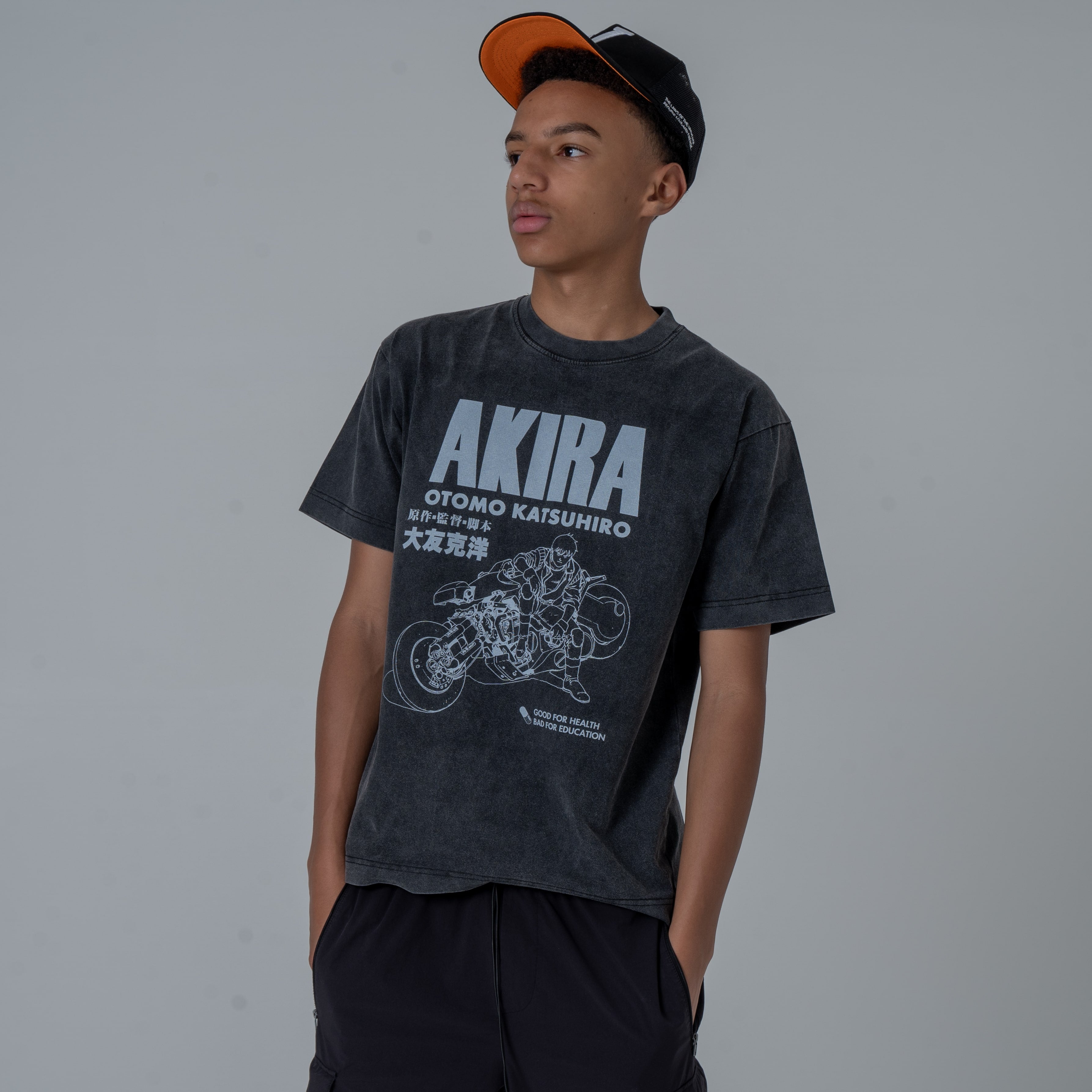 Half-body shot of a male model in a studio wearing a black vintage-washed anime T-shirt featuring a white graphic of Kaneda from Akira.